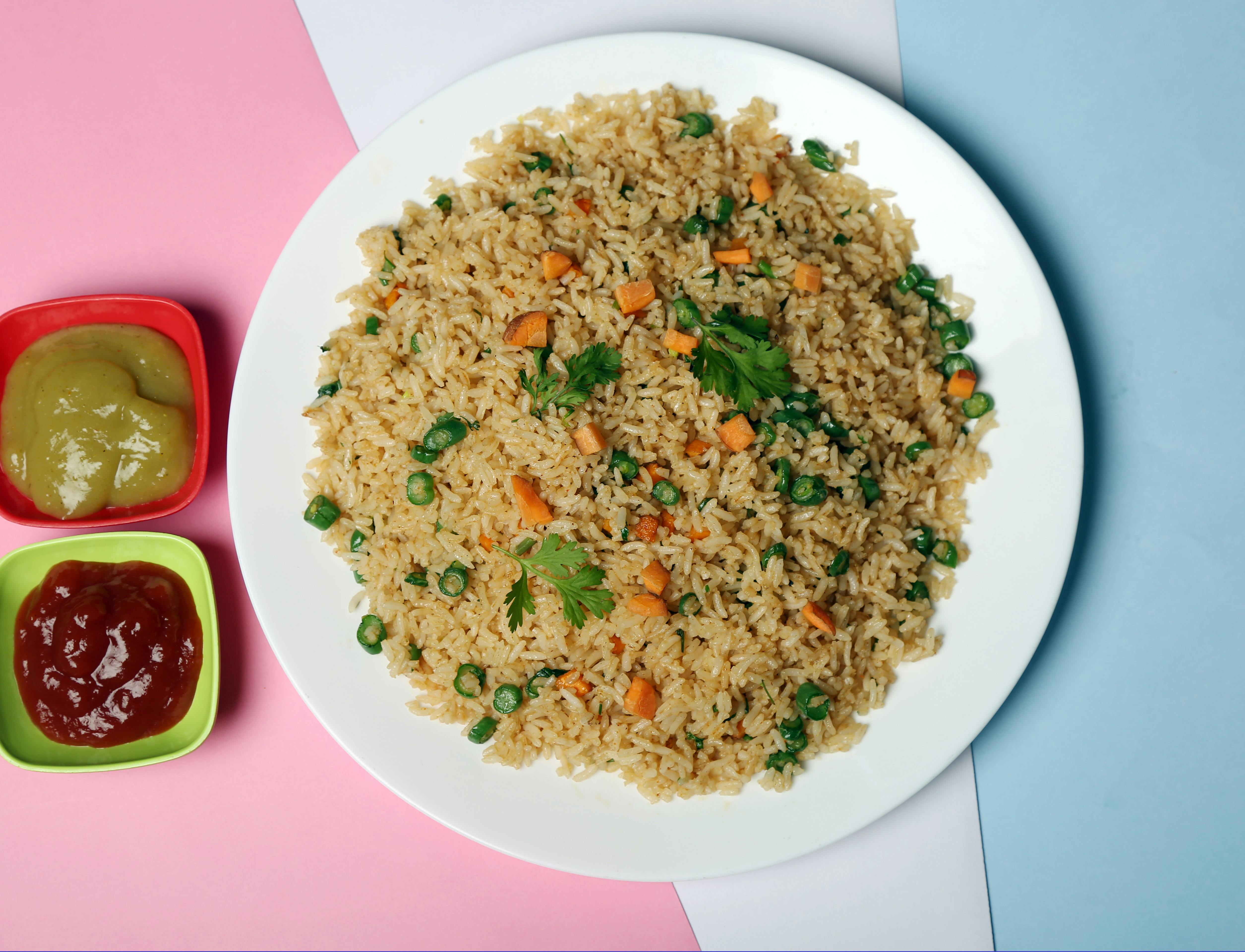 Delicious vegetable fried rice served with green and red sauces, displayed on a colorful background.